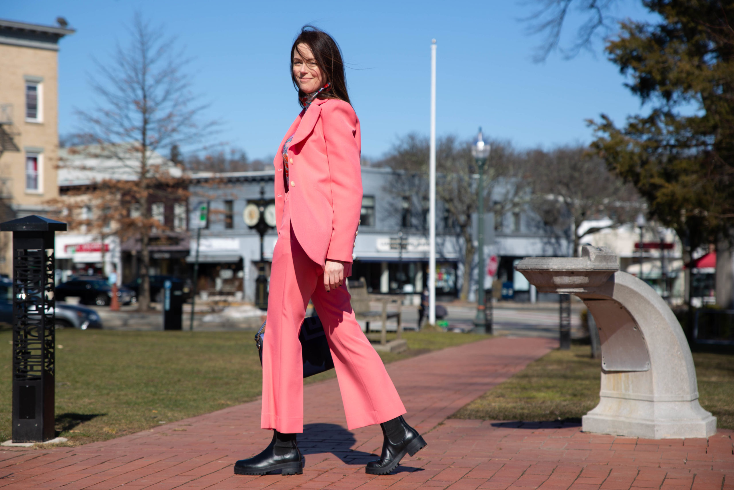conscious citizen wears bright pink suit by stine goya worn with bright floral turtle neck top by the kit outside sunny day blue sky