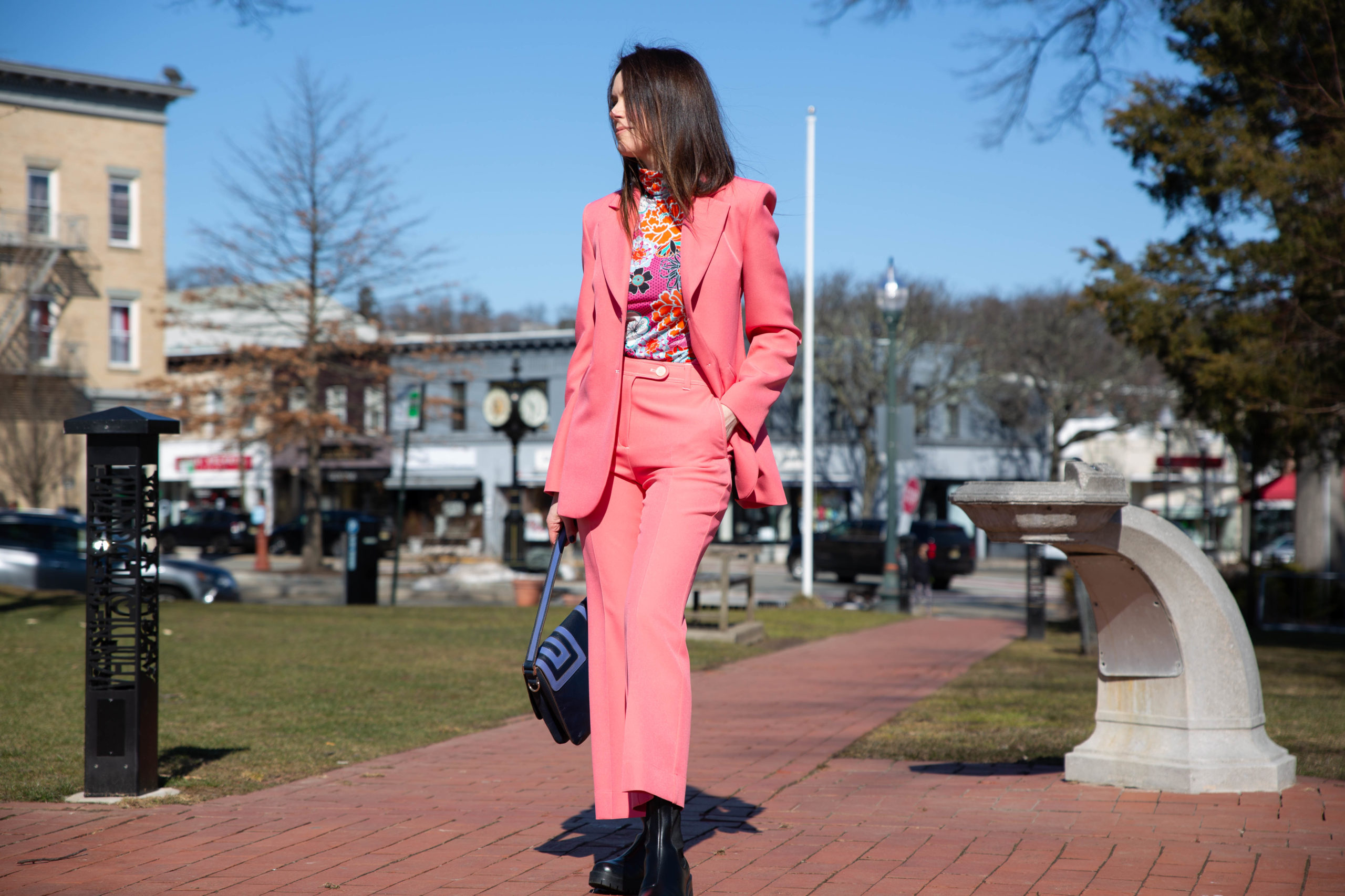 woman wears bright pink suit by stine goya worn with bright floral turtle neck top by the kit outside sunny day blue sky