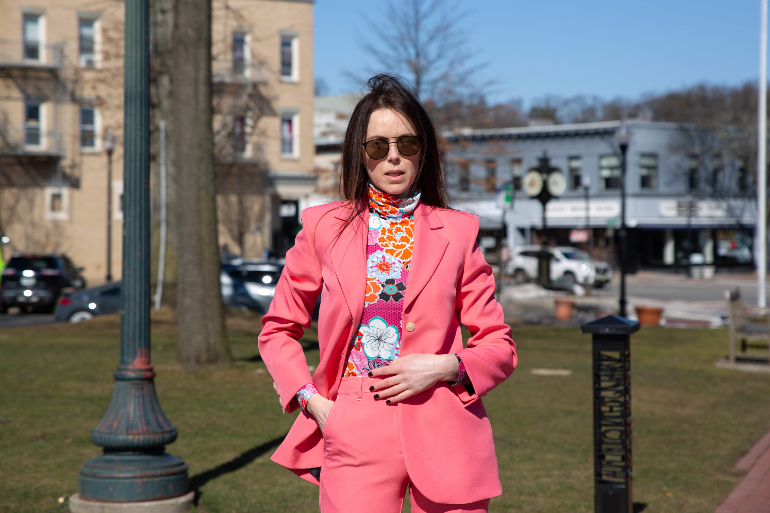 conscious citizen wears bright pink suit by stine goya worn with bright floral turtle neck top by the kit outside sunny day blue sky