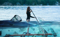 woman on paddleboard on a lake at dusk wading through plastic waste